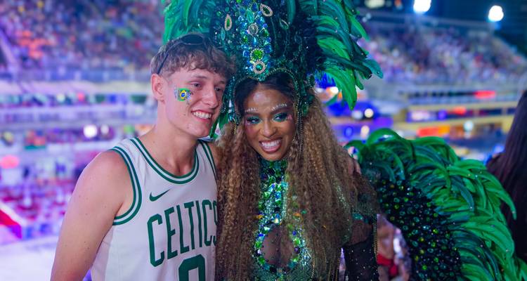 Turista posando con una bailarina de carnaval elaboradamente disfrazada con llamativas plumas verdes y lentejuelas