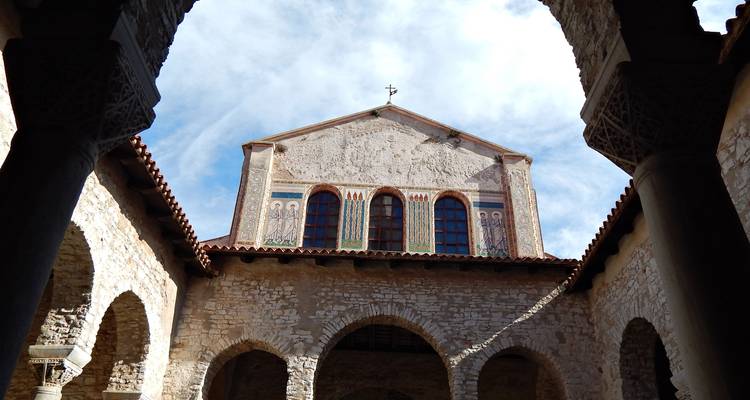 Fachada decorada de una capilla histórica vista a través de arcos de piedra de un patio interior.