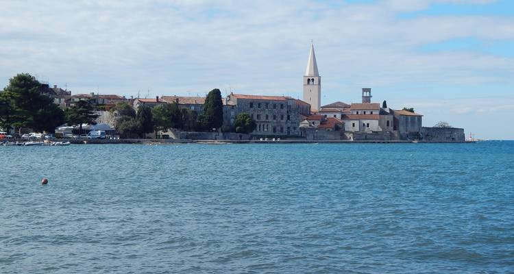 Pueblo costero croata con un esbelta torre de iglesia que se extiende hacia un tranquilo mar azul.
