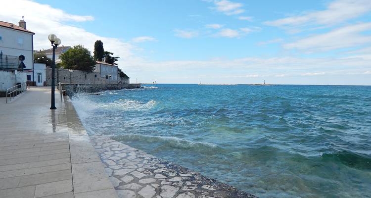 Strandpromenade mit Wellen, die gegen den Steinweg neben türkisfarbenem Wasser spritzen.