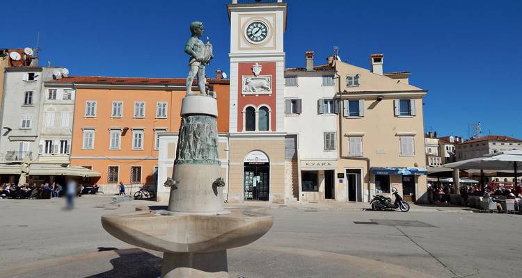 Sonniger Marktplatz mit Brunnen, Uhrturm und farbenfrohen Fassaden in Rovinj.