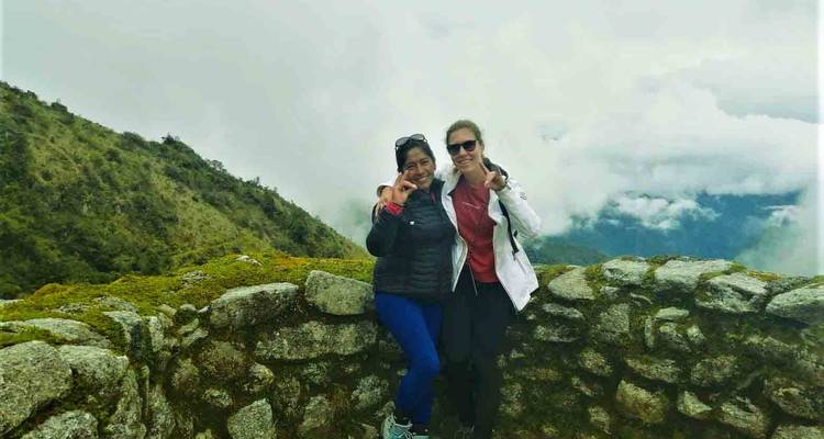 Twee vrouwen poseren op een stenen constructie met uitzicht op een bewolkte vallei.