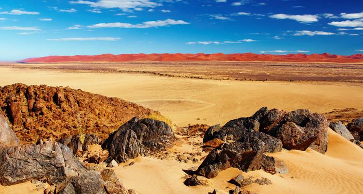 Breed woestijnlandschap met rode zandduinen en rotsen.