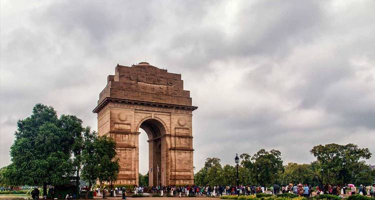 India Gate aufgenommen mit einer Menschenansammlung darunter unter einem bewölkten Himmel.