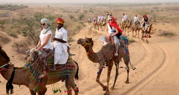 Eine Gruppe von Menschen, die auf Kamelen in einer Wüstenlandschaft reiten.