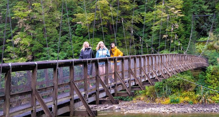 Tres personas caminando por un puente colgante rodeado de exuberante vegetación.