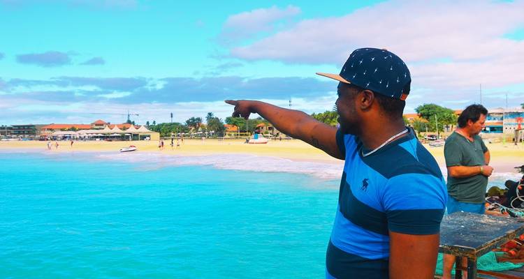 Man die naar de oceaan wijst met een strand op de achtergrond.