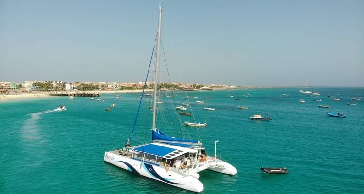 Een catamaran op de oceaan met mensen en een kustlijn.
