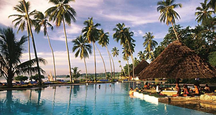 Resort pool area with palm trees and people relaxing.