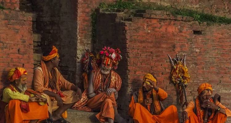 Group of holy men in traditional attire sitting by a brick structure.