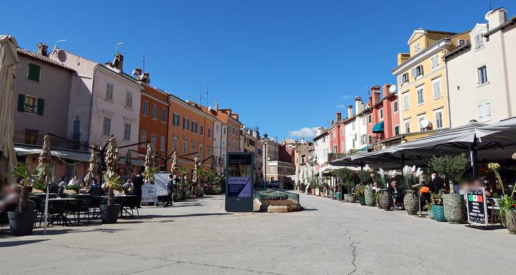 Rue piétonne animée bordée de cafés, de façades colorées et de places assises en plein air par une journée dégagée.