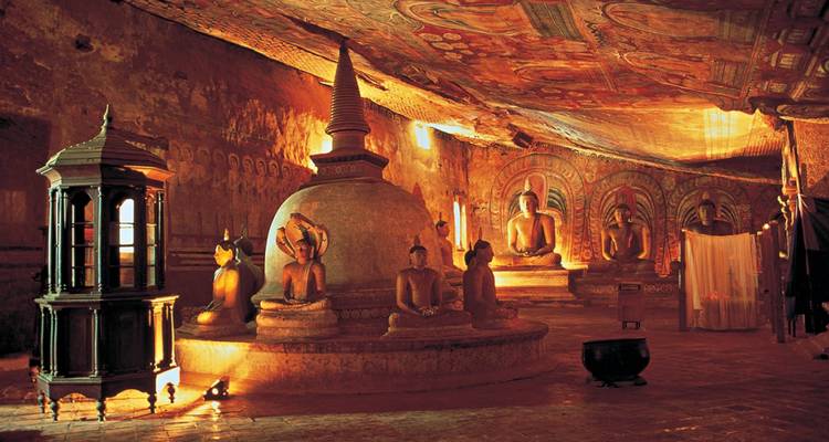 Intérieur d'une grotte avec des statues et un stupa, éclairé chaleureusement.