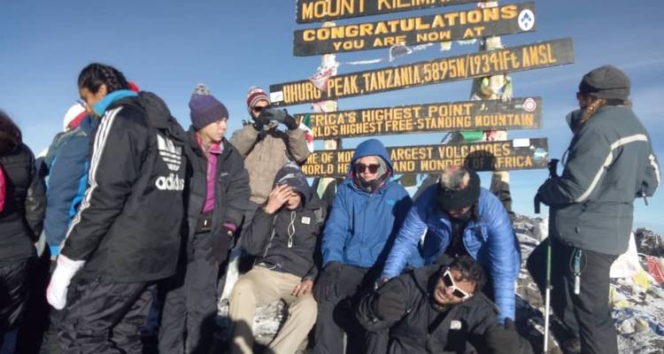 Eine Gruppe von Bergsteigern versammelte sich an einem Schild, das einen Berggipfel anzeigt.
