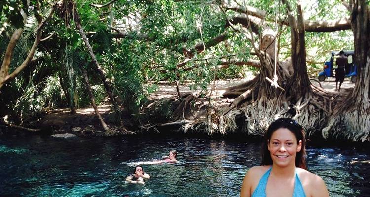 Eine Person, die lächelt, während sie in der Nähe eines natürlichen Pools posiert.