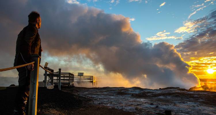 Persona de pie cerca de vapor geotérmico al atardecer.