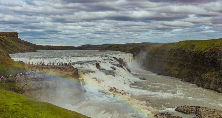 Turistas observando una gran cascada con un arcoíris en lo alto.