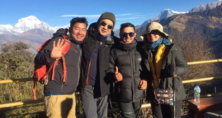 Vier Personen, die mit Daumen-hoch-Geste vor einer bergigen Landschaft posieren.