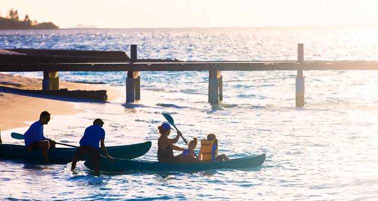 People kayaking on the ocean near a pier during sunset.