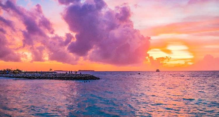 Vibrant sunset over the ocean with clouds and a distant boat.