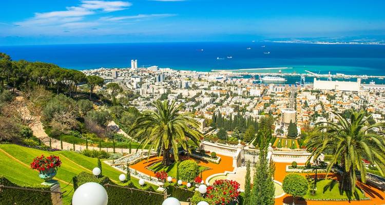 Panoramisch uitzicht vanaf een heuveltop met tuinen en een kuststad eronder.