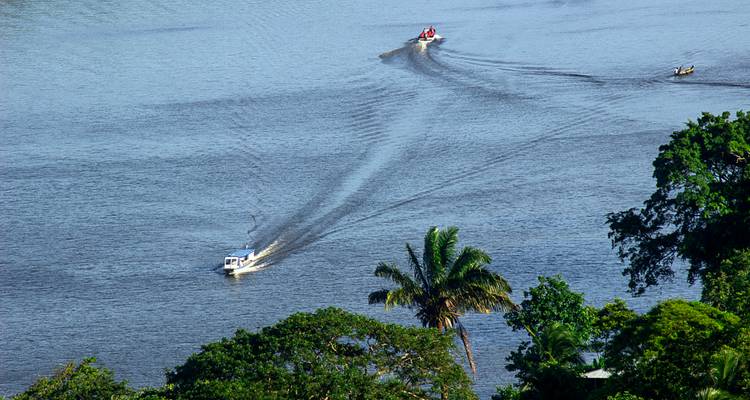 Deux petits bateaux à moteur laissant des sillages blancs sur un large fleuve tropical vus d'en haut