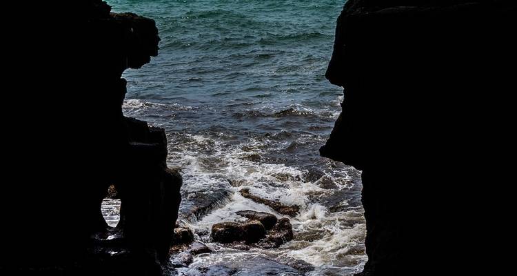 Ocean waves crashing against jagged rocks in silhouette.