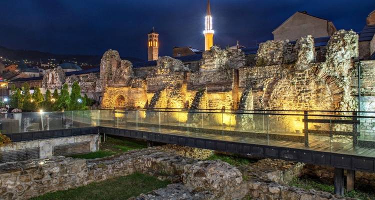 Ruinen mit beleuchtetem Moscheeminarett in der Nacht.