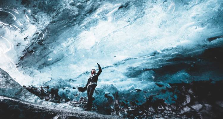Un aventurier pose de manière ludique sous les parois de glace bleue qui s'étendent à l'intérieur d'une grotte glaciaire.