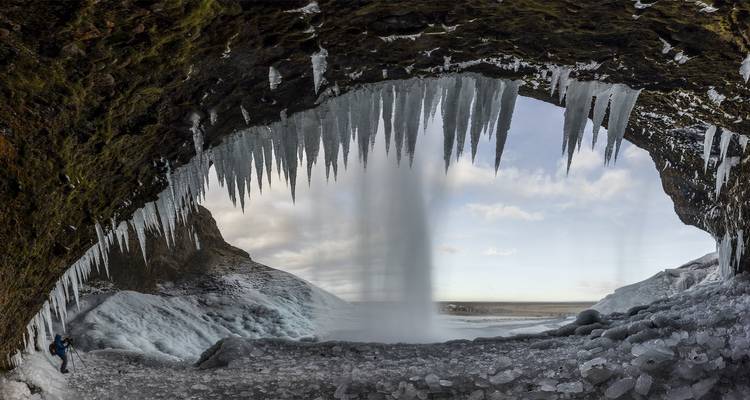 Icicles hang from a cave framing a frozen waterfall at Seljalandsfoss in winter.