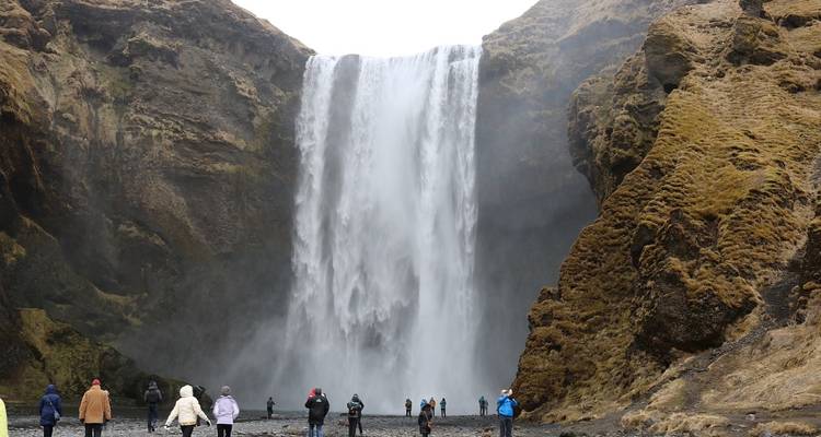 Visitors walk across black sand toward the powerful Skogafoss waterfall crashing into the canyon.