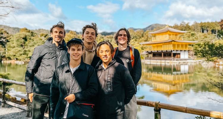 Un groupe de jeunes hommes pose joyeusement devant le pavillon doré Kinkaku-ji reflété dans son étang