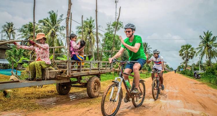 Cyclistes passant devant des habitants assis sur une charrette en bois sur une route rurale.