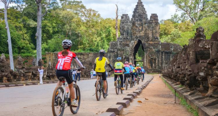 Des cyclistes approchant d'une arche de pierre historique entourée de statues.