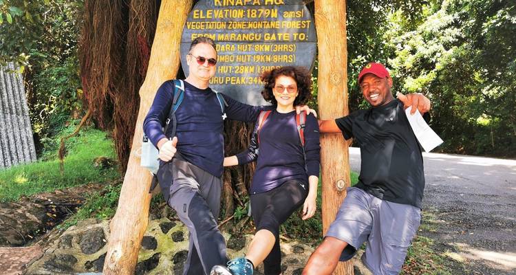 Drei Personen posieren vor einem Schild des Kilimanjaro-Nationalparks.