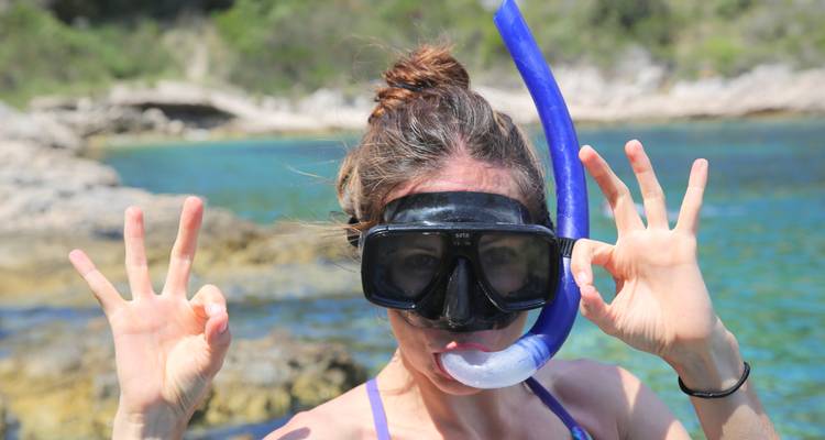 Persona haciendo snorkel con máscara de buceo y tubo respirador, haciendo la señal de OK.