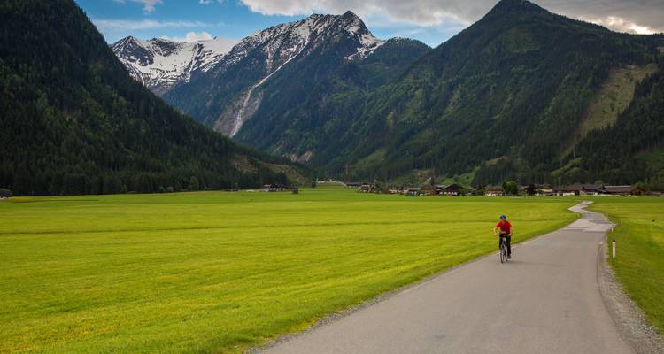 Cycliste sur un sentier à travers une vallée luxuriante flanquée de montagnes.