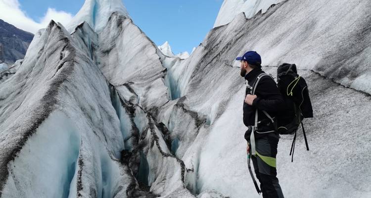 Un grimpeur de glace examine les crevasses dramatiques d'un glacier bleu sous un ciel dégagé.