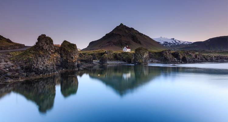 Village côtier tranquille avec un cottage blanc se reflétant dans une eau bleue immobile au crépuscule.