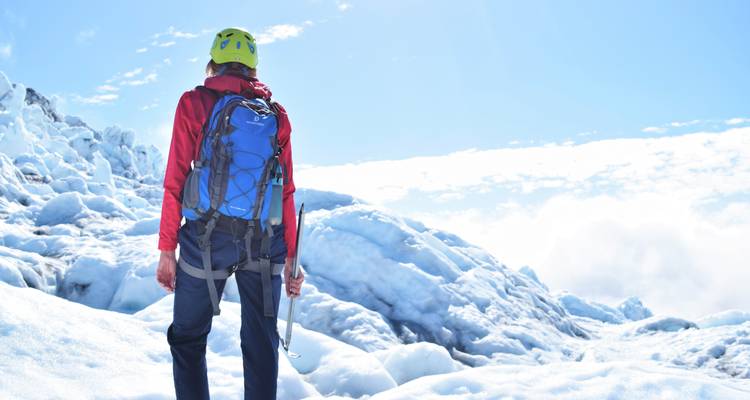 Un alpiniste avec un piolet se tient sur un paysage de glacier brillant de soleil sous un ciel radieux.