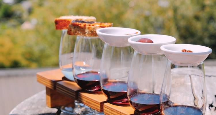 Verres à vin sur une planche de dégustation en bois avec un vignoble vert en arrière-plan.