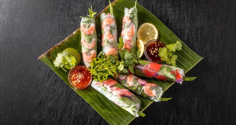 Rouleaux de printemps vietnamiens servis avec sauce de trempage et garnitures sur une feuille.