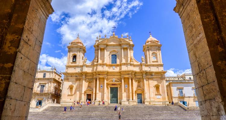 Baroque cathedral with a grand staircase and people in front.