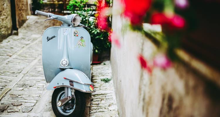 A Vespa scooter parked in a narrow, cobblestone alleyway.