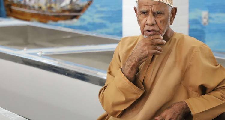 Retrato de un hombre anciano vestido con atuendo tradicional omaní sentado en interiores.
