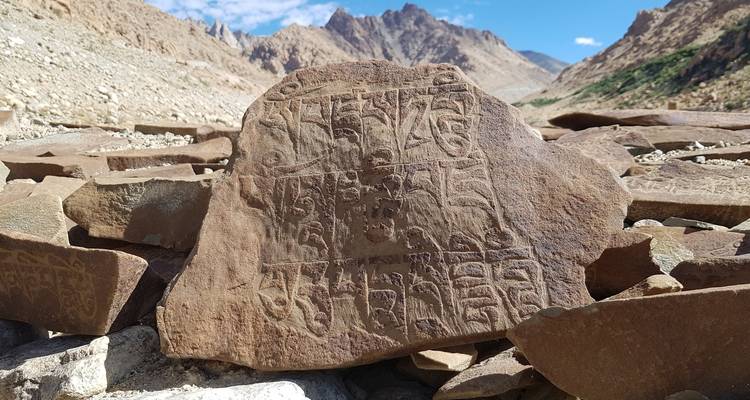 Pierre sculptée ancienne avec inscriptions dans un paysage rocheux.