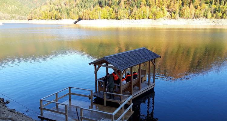 People on a wooden boat floating in a peaceful lake surrounded by mountains.