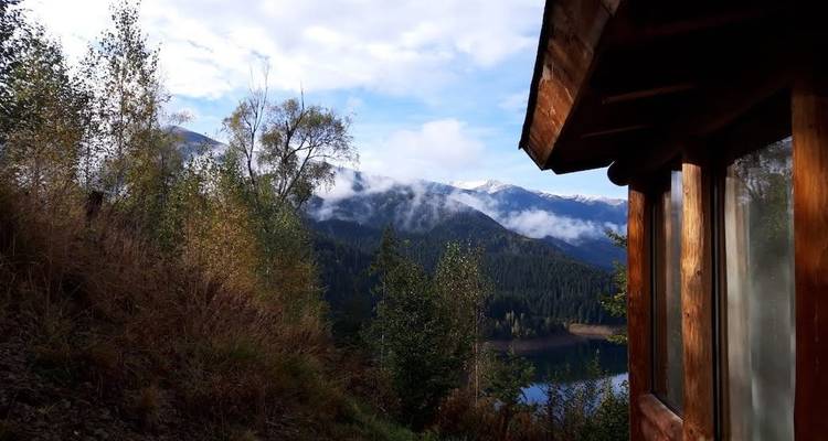 Mountain cabin overlooking a forested valley and distant mountain peaks.