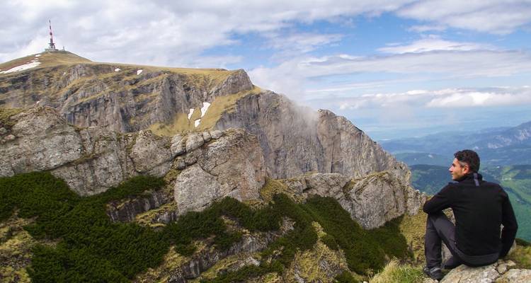 Man sitting at a clifftop with panoramic mountain views.