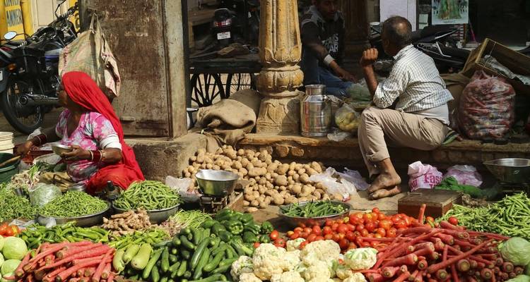 Deux personnes à un marché de légumes avec divers produits frais.