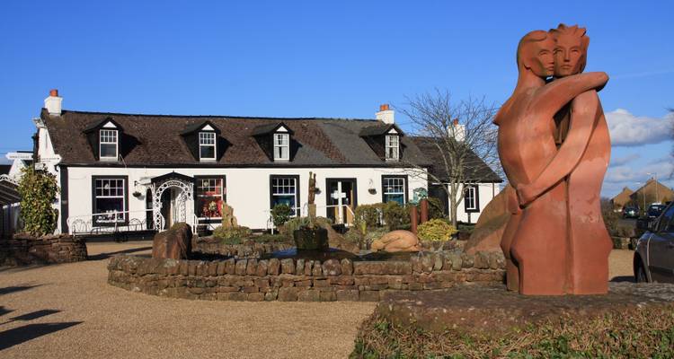 Gretna Green met een historisch gebouw en beeldhouwwerken in een tuinomgeving.